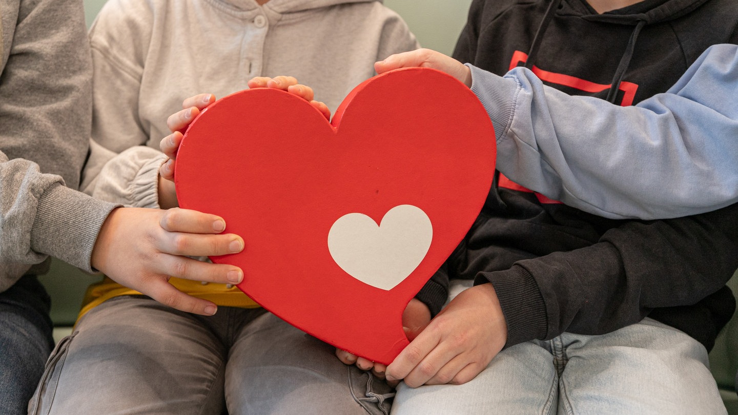 Vier Kinder halten gemeinsam ein rotes Herz.