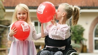 Zwei Mädchen mit roten Luftballons, eins schaut in die Kamera