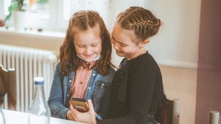 Zwei Mädchen schauen etwas auf einem Smartphone an (nur im Zusammenhang mit Herzenssache verwenden!)