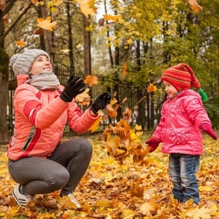 Frau spielt mit kleinem Mädchen im Herbstlaub.