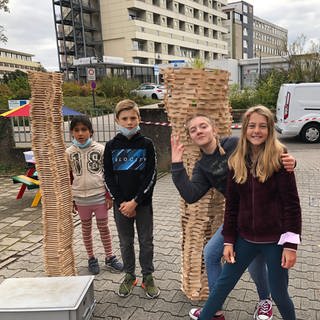 Kinder spielen vor zwei großen Türmen aus Bauklötzen.