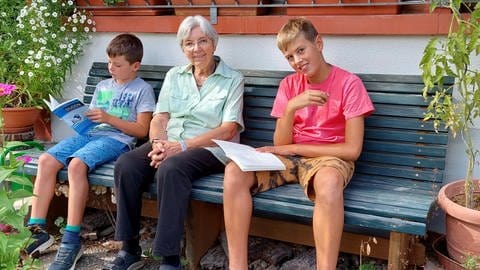 Zwei Jungs sitzen neben einer älteren Dame auf der Bank