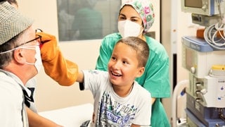 Ein Junge zwickt einem Klinikclown in seine rote Nase.