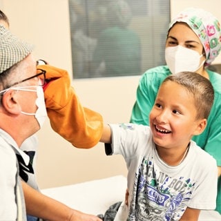 Ein Junge zwickt einem Klinikclown in seine rote Nase.